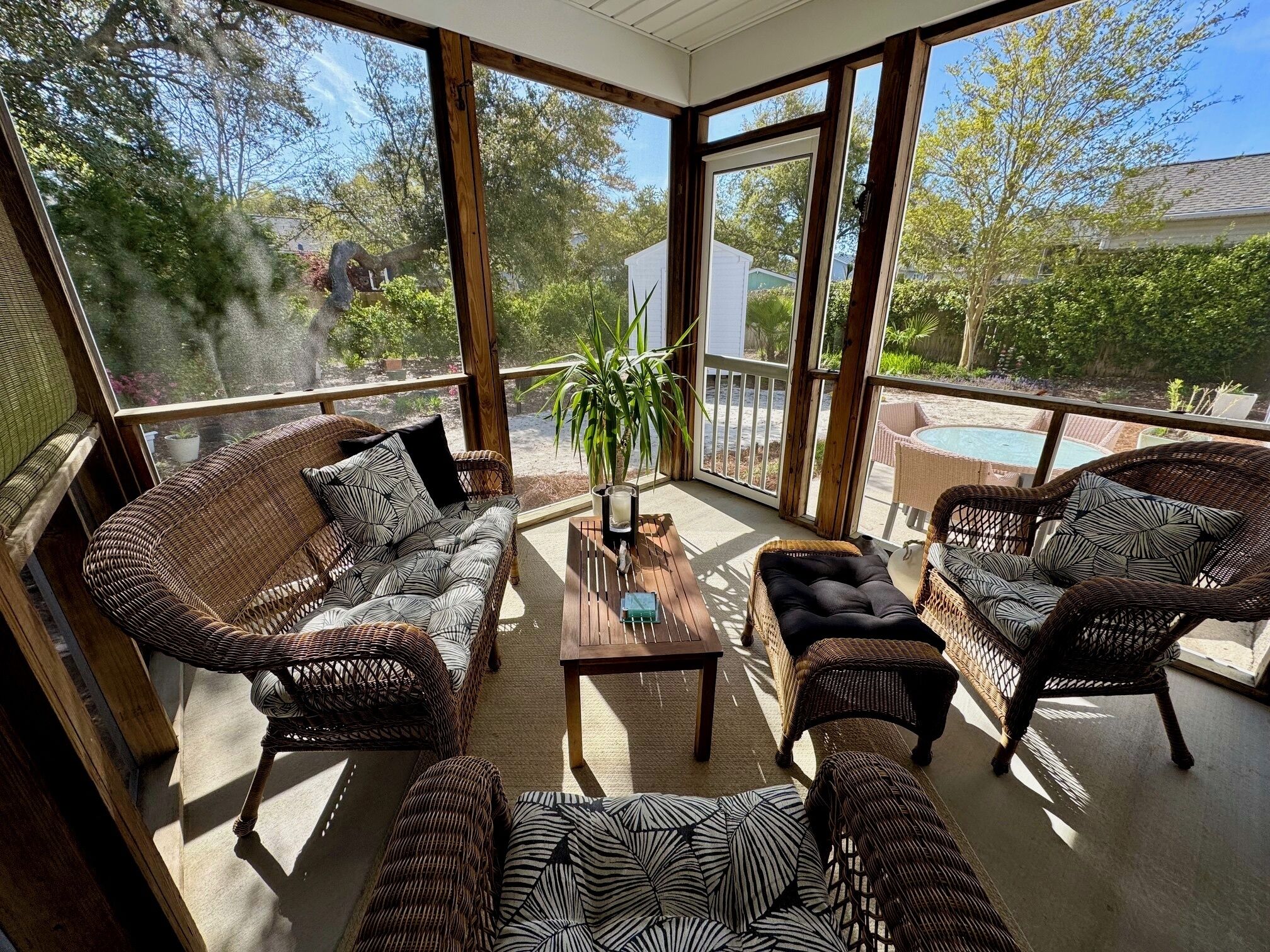 Een zonnig terras met rieten meubilair, een bijzettafeltje en uitzicht op een zwembad en groen.