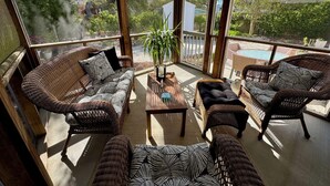 Un patio soleado con mobiliario de mimbre, una mesa de centro y vistas a una piscina y follaje.
