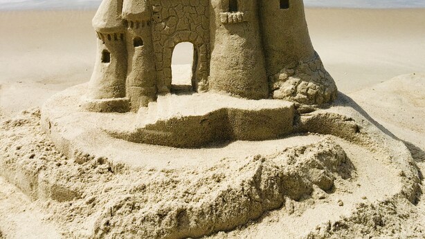 Un castillo de arena con múltiples torres y un arco central en la playa.