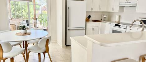 A modern kitchen with white cabinetry, a central island, and a dining area with a round table and chairs.