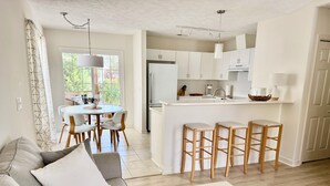 Una cocina moderna con armarios blancos, una isla central con taburetes y un comedor con mesa y sillas.