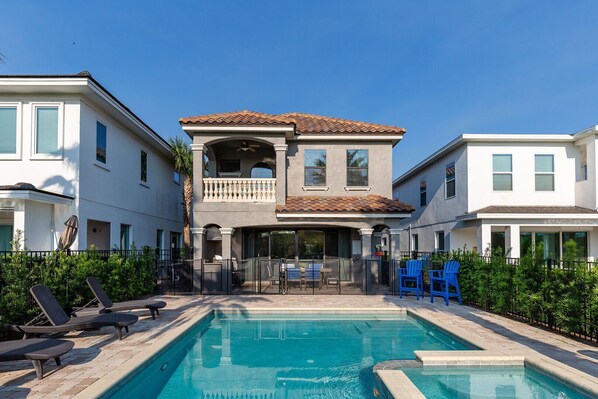 A two-story house with a pool, a balcony, and a fenced patio area with lounge chairs. - Ultimate Family Escape | 5BR Fun Home w/ Private Pool, Arcade, and Themed Kids' Room Near Disney (Kissimmee)