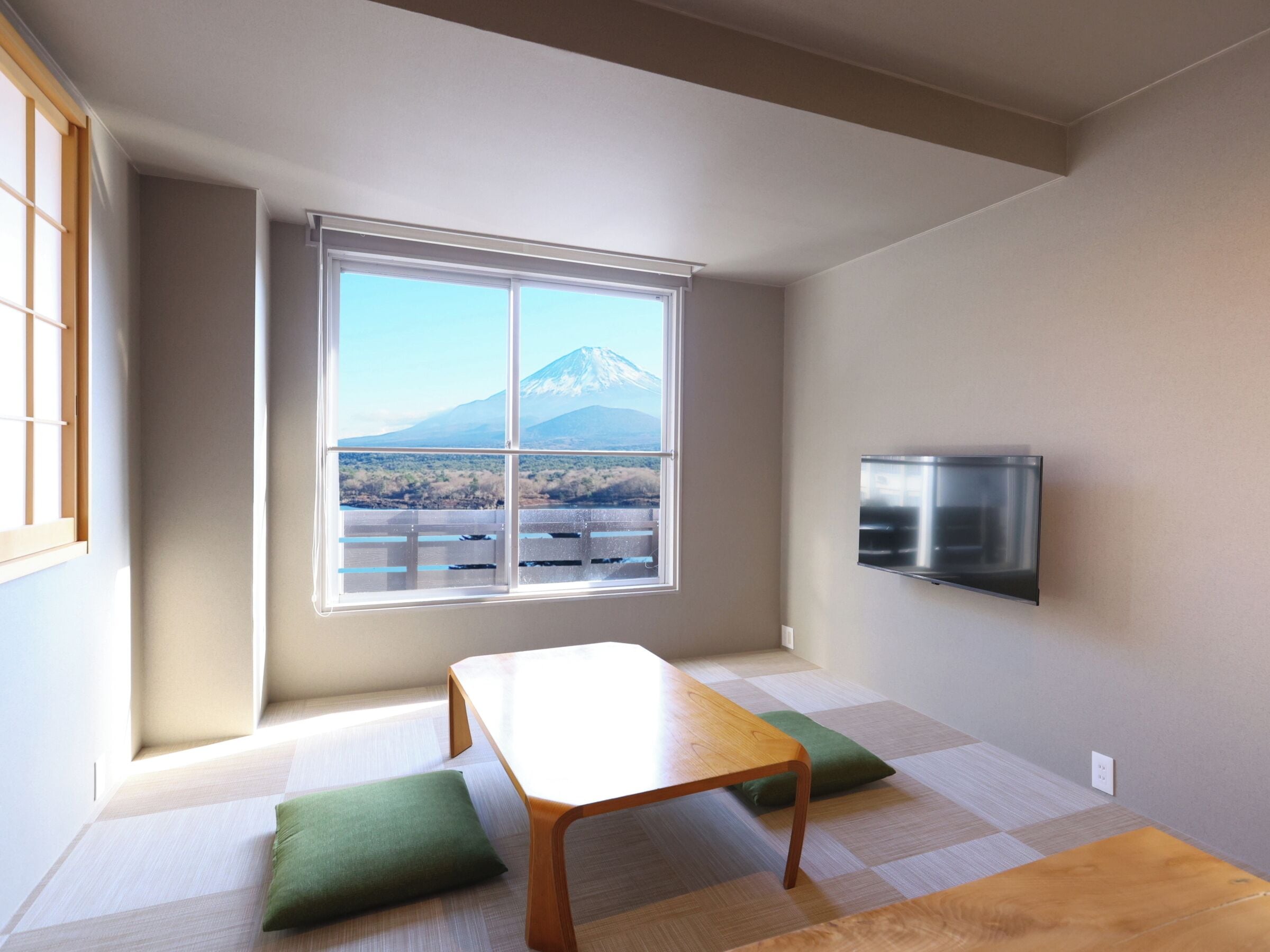 Una habitación con una mesa, cojines verdes, un televisor y una ventana con vista a la montaña.