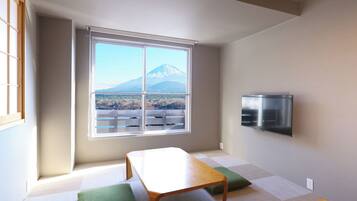 Una habitación con una mesa, cojines verdes, un televisor y una ventana con vista a la montaña.