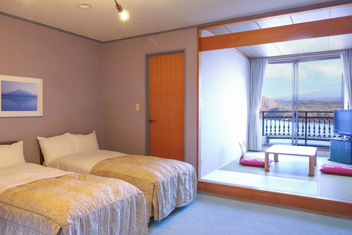 Quarto de hotel com duas camas, uma janela ampla com vista, uma varanda pequena e uma televisão.