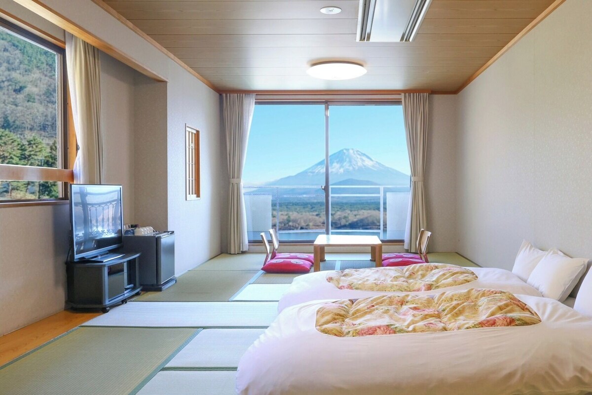 Quarto de hotel com cama, televisão, escrivaninha e vista para uma montanha.