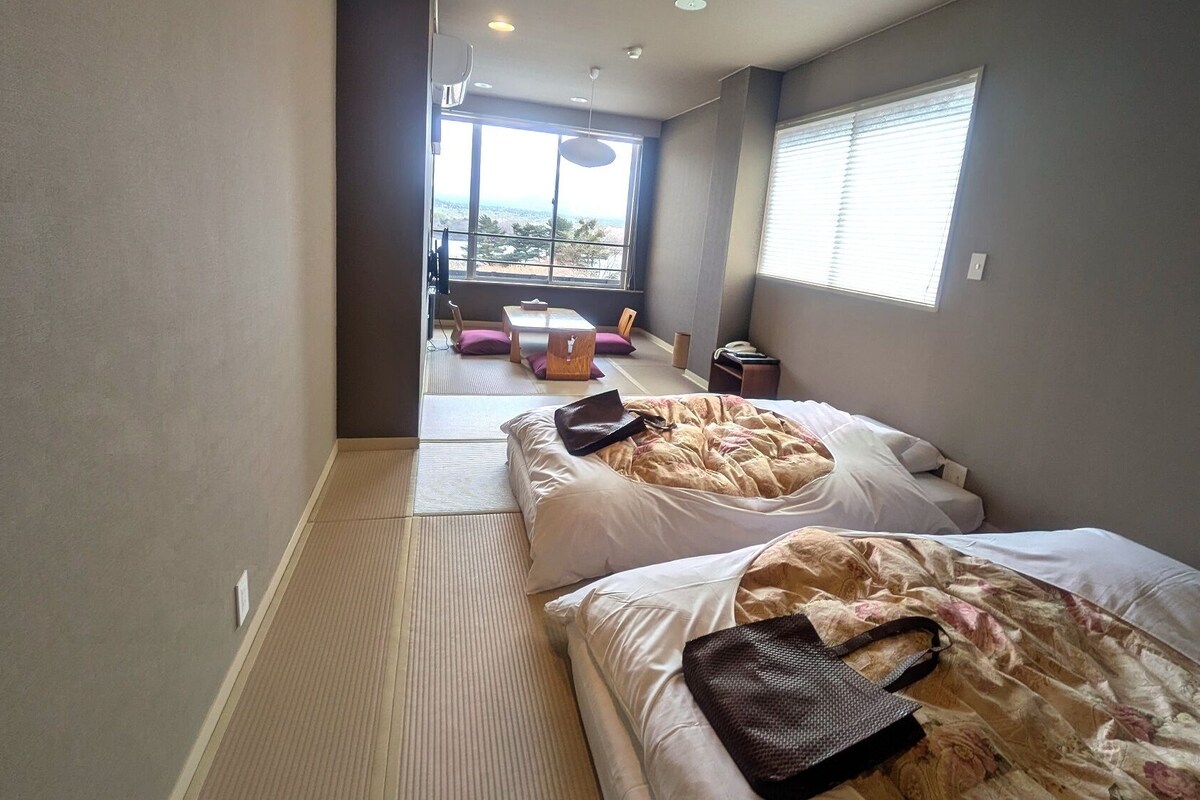 Quarto de hotel com duas camas, vista através de uma grande janela e chão com tatame.