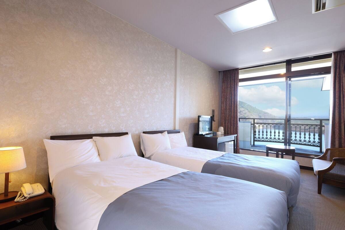 Habitación de hotel con dos camas, un escritorio, una silla, un teléfono y un amplio ventanal con vista al mar.