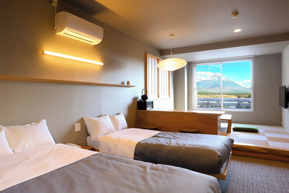 Quarto de hotel com duas camas, uma janela grande com vista para as montanhas, ar condicionado e uma prateleira fixada na parede.