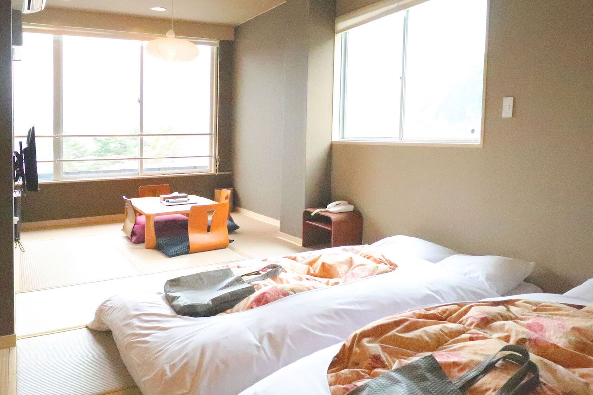 Um quarto com uma cama, uma mesinha, cadeiras e uma janela.