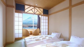 Een hotelkamer met een groot bed, twee stoelen, uitzicht op een berg en traditionele Japanse schuifdeuren.