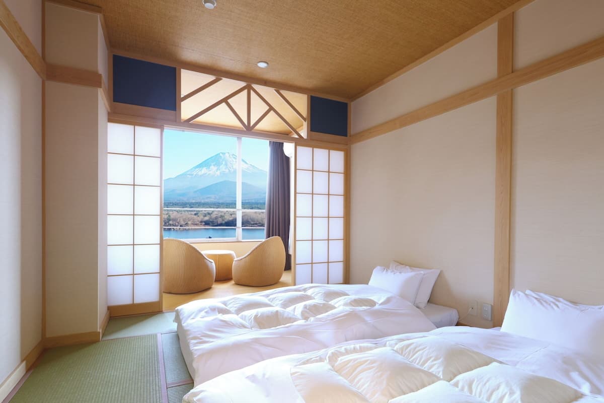 Habitación de hotel con una cama grande, dos sillas, vista a una montaña y puertas correderas tradicionales japonesas.