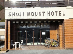 The exterior of the Shoji Mount Hotel with a sign above the entrance, a glass door, and a bicycle rack outside. - Shoji Mount Hotel (Fujikawaguchiko)