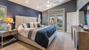 Une chambre à coucher comprenant un lit, une table de chevet, une lampe, un ventilateur de plafond et une vue sur l’extérieur grâce à une porte vitrée.