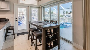 Une cuisine moderne avec un coin repas, de grandes fenêtres et une vue sur une piscine et un espace de détente extérieur.