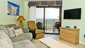 A living room with a sofa, armchair, table, and dresser. A TV is mounted on the wall, and a painting is on the wall. - Sea View at Sand Dunes Resort (Myrtle Beach)