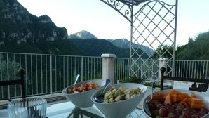 A table with bowls of fruit and a glass of water, set against a scenic mountain backdrop. - Le Mont D'olivine (Utelle)