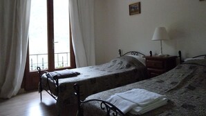 A bedroom with two single beds, a nightstand with a lamp, a window with curtains, and a small painting on the wall. - Le Mont D'olivine (Utelle)