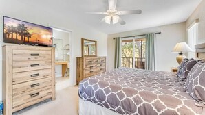 Un dormitorio con cama, cómoda, televisor, ventilador de techo y balcón con vistas.