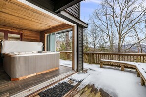 Una terraza de madera con un jacuzzi, un banco y vistas a árboles y montañas.
