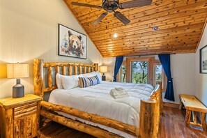 A wooden-framed bed with a headboard, a bedside table with a lamp, and a view of the outdoors through a window.