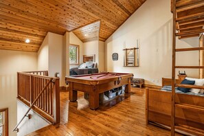 Una habitación con piso de madera, mesa de billar, camas literas y zona de altillo.