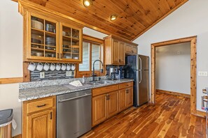 A kitchen with wooden cabinets, a stainless steel dishwasher, a refrigerator, and a coffee maker. - 10 Min to Banner Elk | Sleeps 19 | Hot Tub, Sauna, Movie Theater & Mountain Views (Banner Elk)