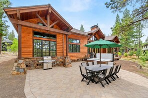 A wooden cabin with a stone foundation, a barbecue grill, and a patio with a table and chairs.