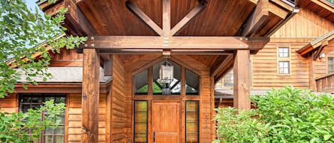 Una cabaña de madera con base de piedra, una puerta de madera grande y un porche cubierto.