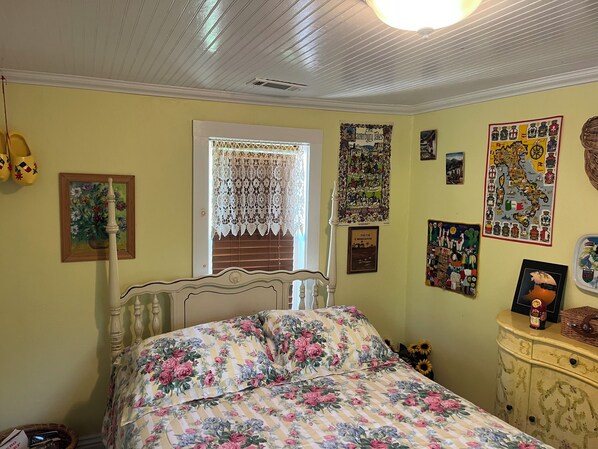 Un dormitorio con colcha estampada, cabecera de madera y ventana con cortinas de encaje.