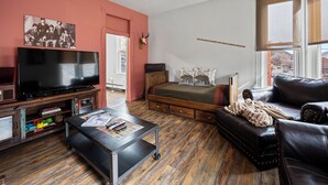 A cozy living room with a television, a sofa, a bed, and a wooden floor.