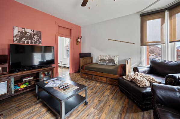 A cozy living room with a television, a sofa, a bed, and a wooden floor.