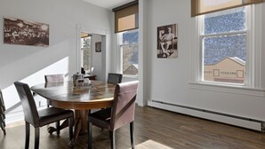 A dining area with a round table, chairs, and a view of a house through a window.
