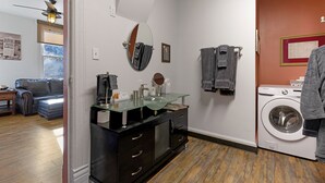 A compact laundry room with a washing machine, a glass-top vanity with a mirror, and a dark-colored cabinet.