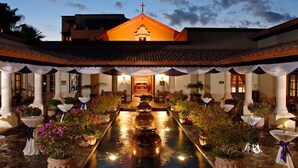 Un patio con una fuente central, rodeado de mesas y sillas, y un edificio con una cruz en la parte superior.