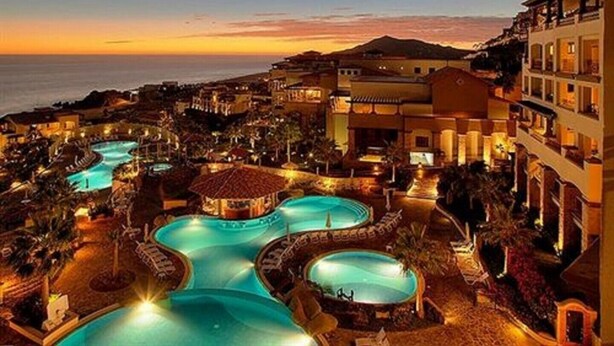 Un resort con varias piscinas, vista a la playa y montañas al fondo.