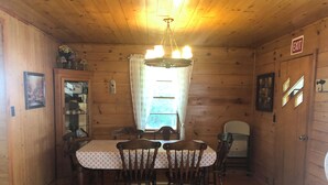 Ein Esszimmer einer Holzhütte mit Tisch und Stühlen, einer Pendelleuchte und einem Fenster mit Vorhängen.