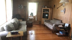 Ein gemütliches Blockhaus-Interieur mit Holzwänden, einer Couch, einem Tisch, einem Fernseher und einer Lampe.