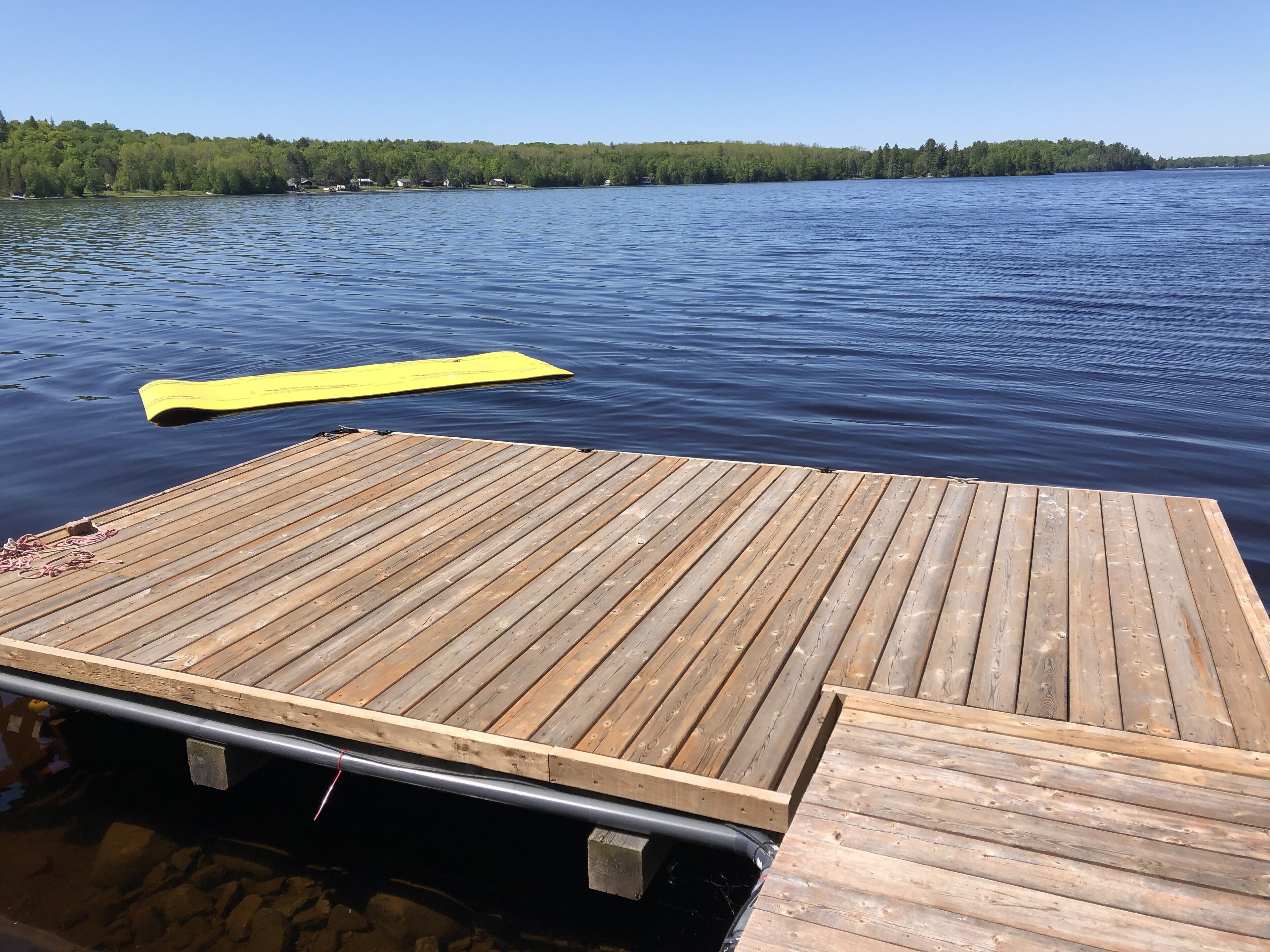 Un muelle de madera se extiende hacia un lago tranquilo donde descansa una tabla de remo amarilla.
