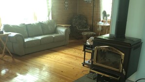 Ein gemütliches Wohnzimmer mit Holzboden, einer Couch, einem Sessel, einem Tisch, einem Kamin und einer Lampe.