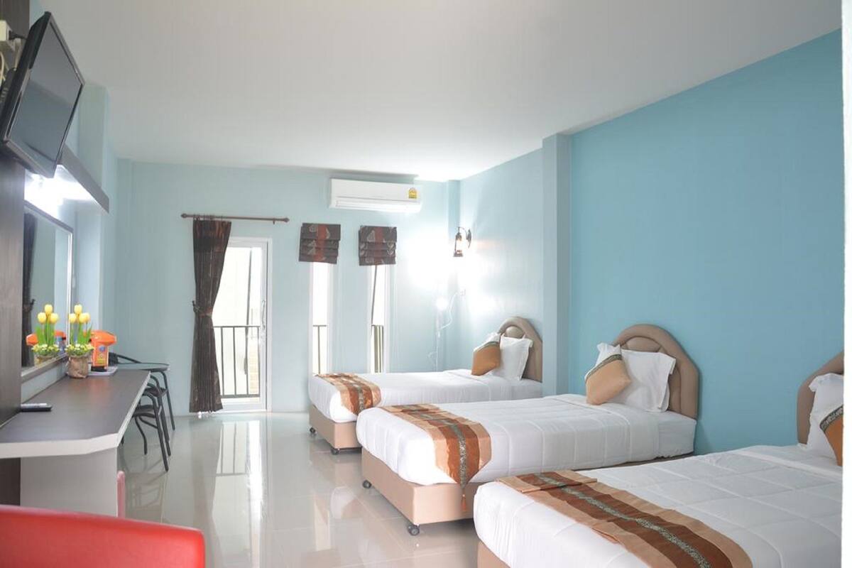 A hotel room with three beds, a desk with a television, and a window with curtains.