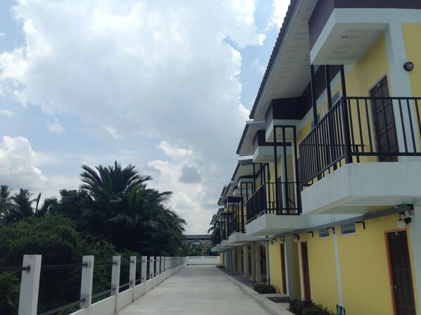 A row of yellow and white buildings with balconies, a concrete pathway, and palm trees in the background. - Satun Boutique Resort (Satun)