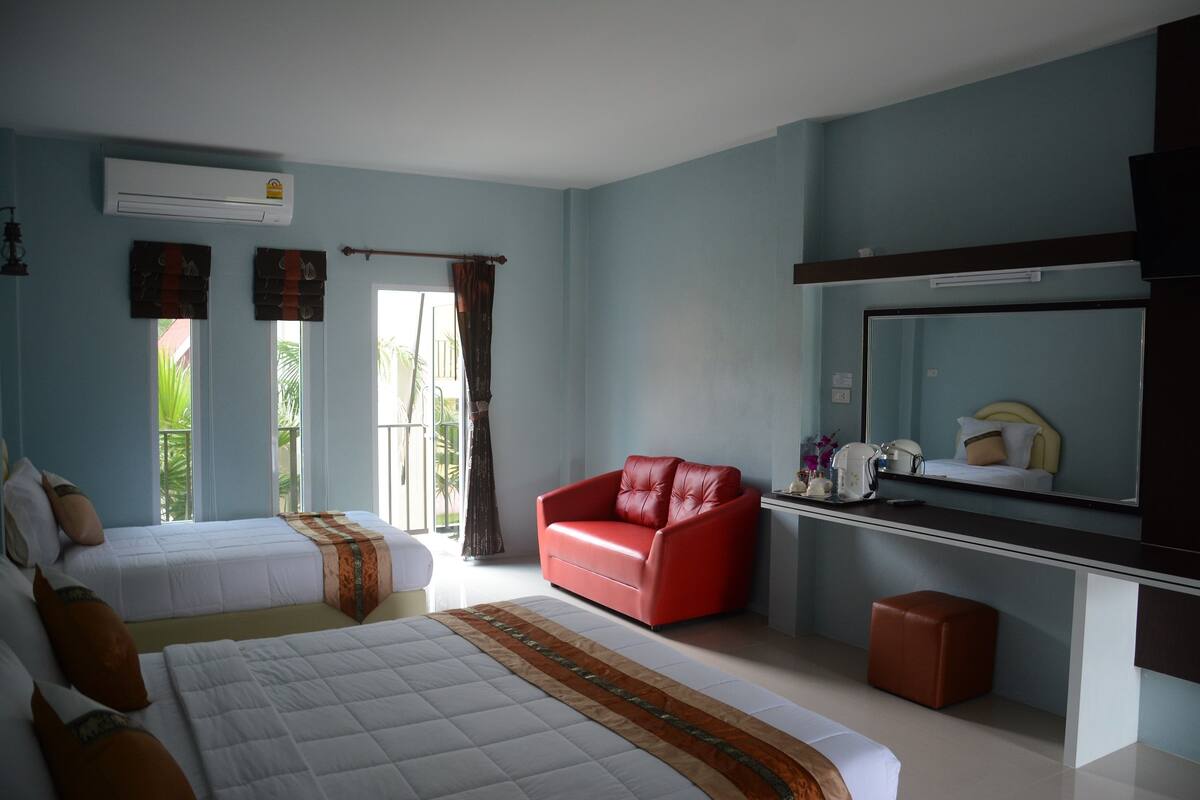 A hotel room with two beds, a red sofa, a large mirror, and a window with curtains.