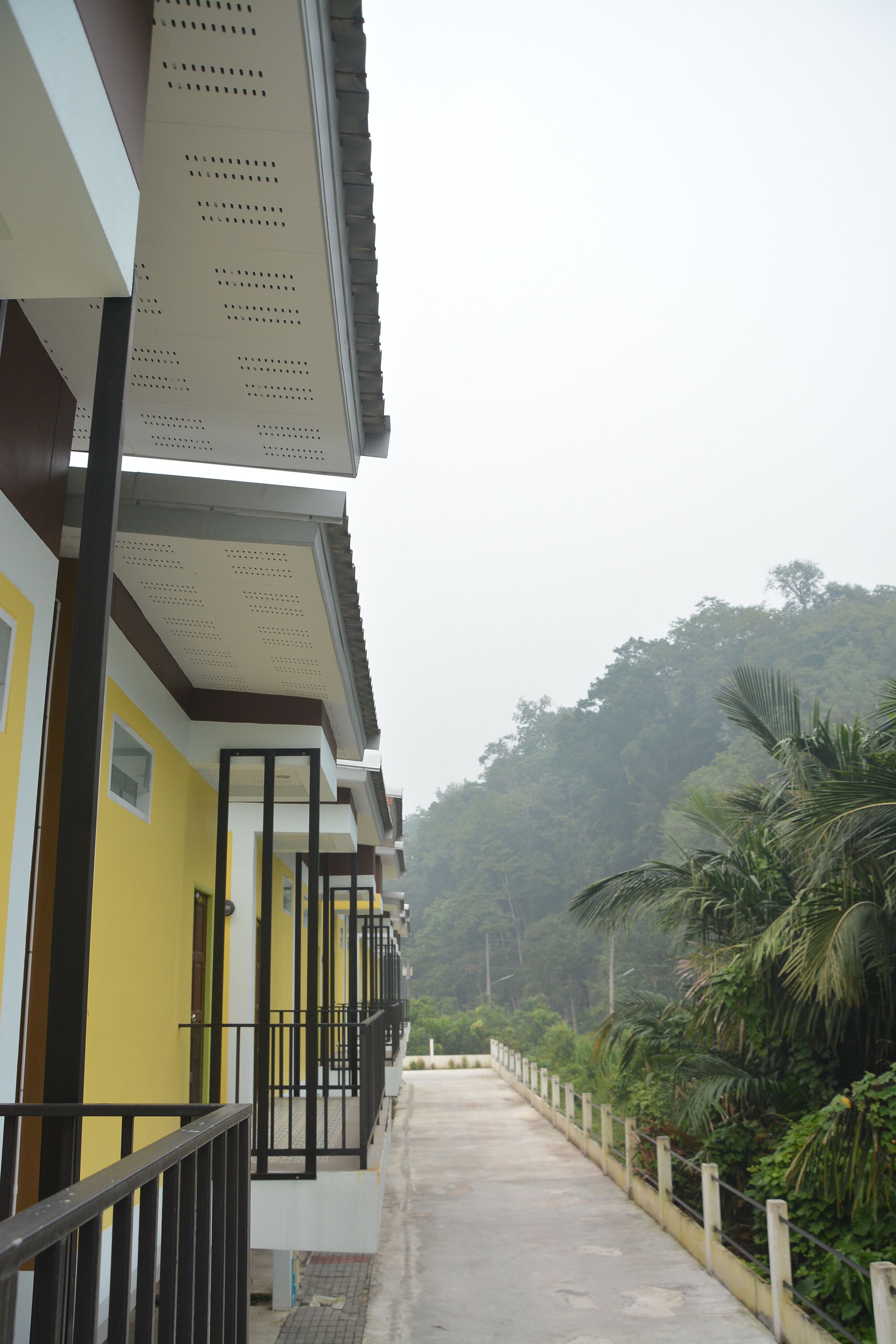 A corridor with balconies, a yellow building, and a view of a forested hill.