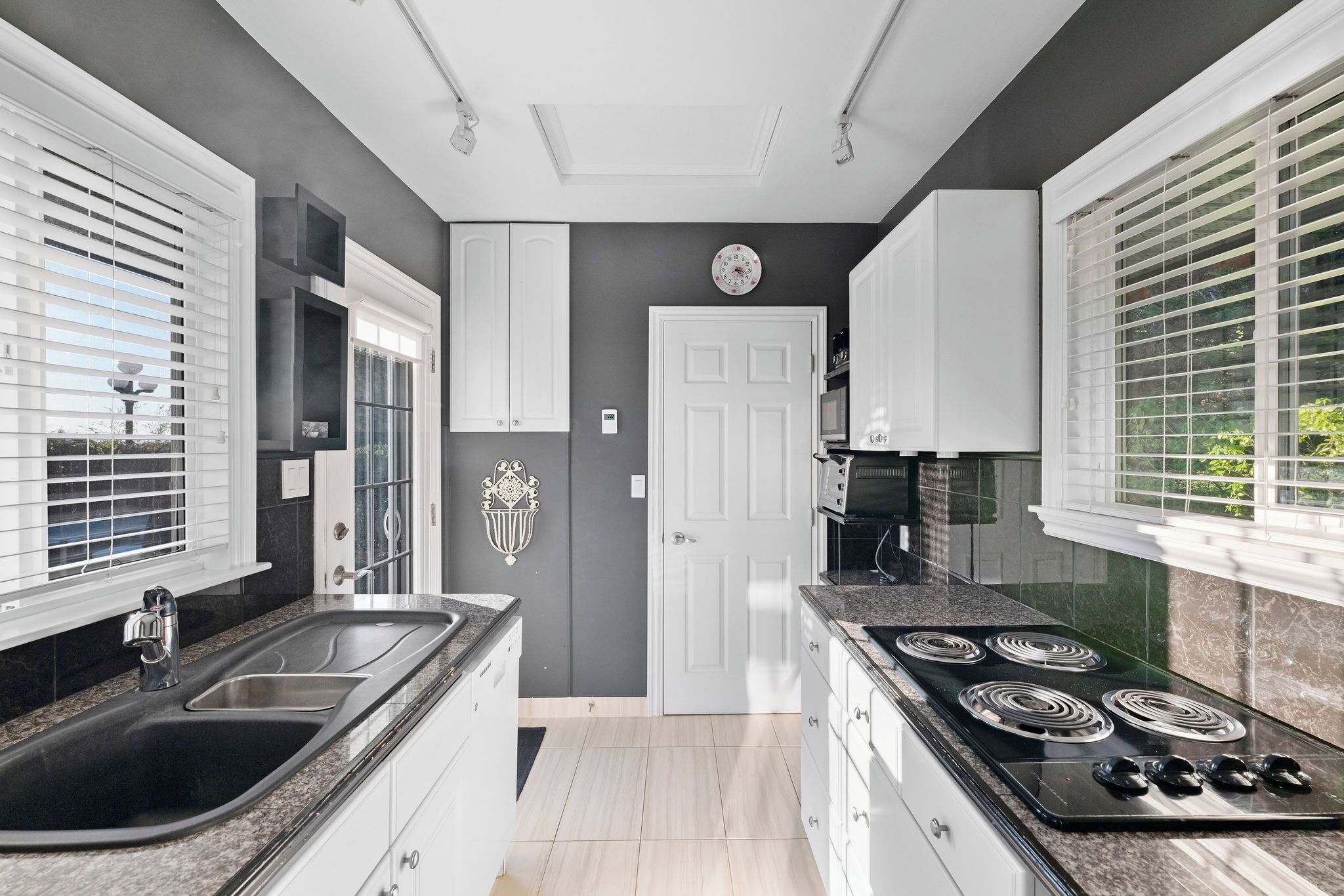 Una cocina moderna con armarios blancos, una estufa negra y un amplio ventanal con persianas.