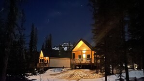 A lodge with a wooden exterior and a balcony, surrounded by snow and trees, with a mountain in the background. - Cozy Fireside Cottage - The Rock (Nordegg)