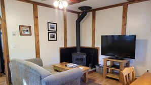 A cozy living room with a sofa, a TV, a wooden table, and a fireplace. - Cozy Fireside Cottage - The Rock (Nordegg)