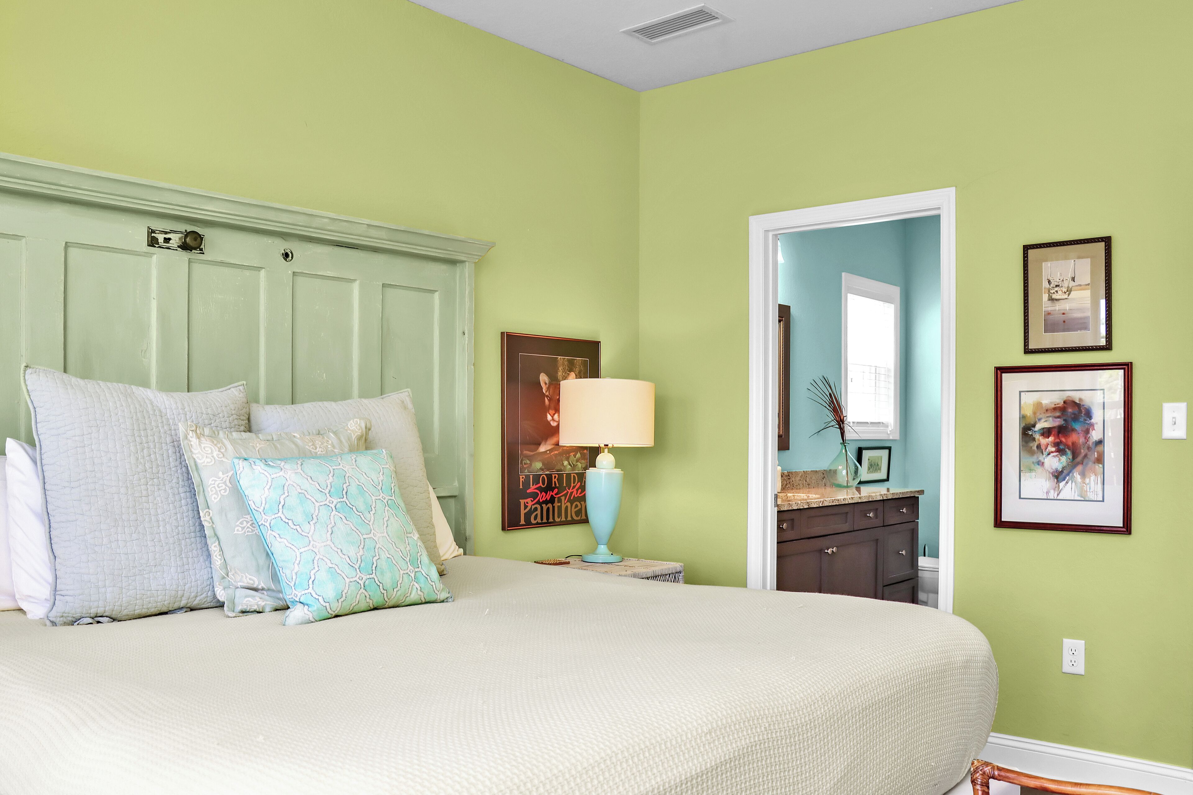 Une chambre à coucher avec un grand lit, une table de chevet, une lampe et une porte donnant sur une autre pièce.