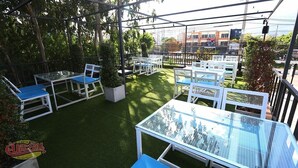 An outdoor patio with multiple tables and chairs, surrounded by greenery and a view of buildings in the background. - Kanith Place (Chiang Mai)
