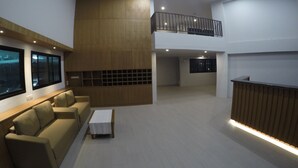 A spacious, modern interior with a high ceiling, recessed lighting, a wooden reception desk, and a seating area with a sofa and a small table. - Kanith Place (Chiang Mai)
